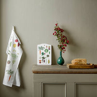 Kitchen setting with a towel, wall art, vase with flowers, and bread on a wooden surface.